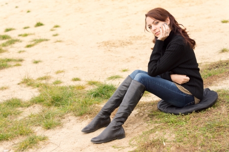 Wistful young woman sitting outdoors alone on a cushion on sandy ground looking at the ground with a sombre expression as she rests her chin on her handの写真素材