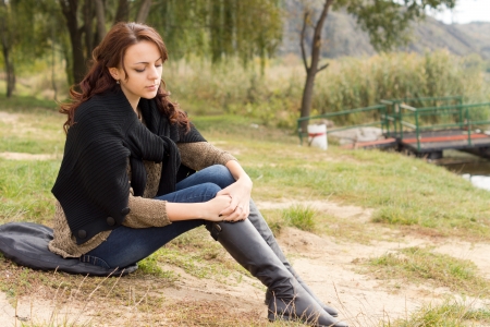 Depressed trendy young woman sitting alone outdoors on a cushion in a park staring morosely down at the groundの写真素材