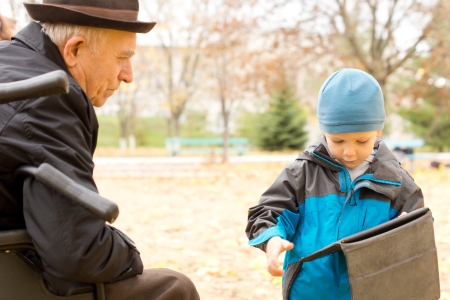 Cute young boy with his grandfather showing him something on his handheld tablet-pc as the two enjoy a day out together in a park or gardenの写真素材