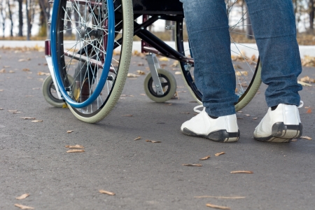 Low angle view from the rear of a person pushing a wheelchair along the street wearing sneakers and jeansの写真素材