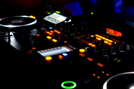 Closeup view at night of the colourful lights on the turntables and music mixing deck at a disco...