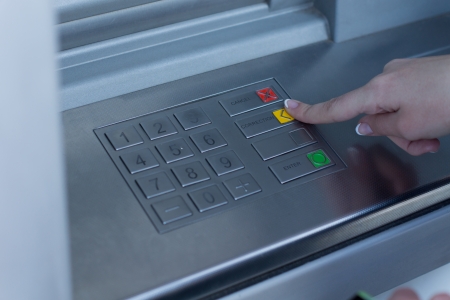 Woman selecting a transaction on a bank ATM depressing the yellow button with her finger enabling her to withdraw cash from the automated tellerの写真素材