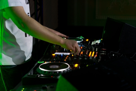 Close up of the hands of a young male disc jockey mixing and blending music tracks on his deck in the darkness of a party or nightclubの写真素材