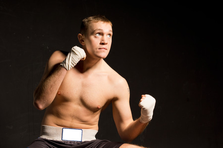 Strong young boxer seeking inspiration as he raises his eyes to the ceiling during a practice or fight while standing with his fists raised on a dark background with copyspaceの写真素材