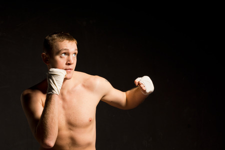 Fit young boxer in training standing in the darkness with his fists raised looking up to the top right corner, with copyspaceの写真素材