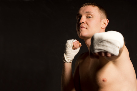 Belligerent young boxer throwing a punch as he eyes up his opponent with an intense expression, focus to his face on a dark background with copyspaceの写真素材