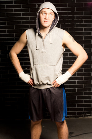 Confident fit young boxer standing waiting with his hands on his hips for the start of his match against a dark brick wallの写真素材