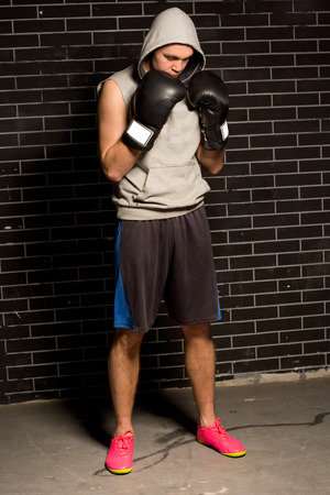 Anxious young boxer standing waiting for his match with his gloved fists raised to his chin as he stares down at the floor in front of a brick wallの写真素材