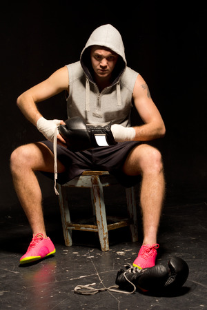 Young boxer sitting on a stool at the side of a ring during training putting on his glovesの写真素材