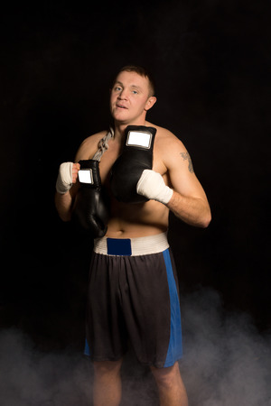 Muscular fit young boxer preparing for a fight standing in the darkness with his gloves slung round...