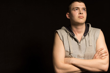Handsome young man lost in contemplation standing with his arms folded looking up into the air with a serious thoughtful expression, dark with copyspaceの写真素材
