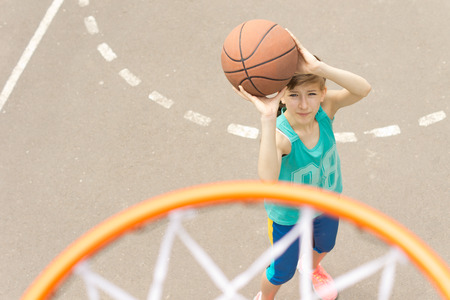 Young girl taking aim at the goal on a basketball court standing with the ball raised aiming at the hoop, view from aboveの写真素材