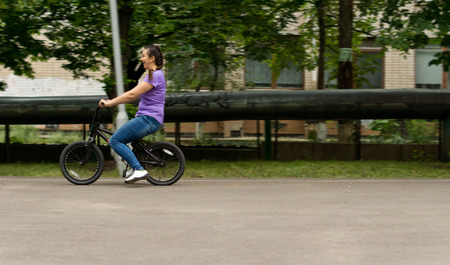 Attractive middle-aged woman riding a kids bicycle which is a few sizes too small for her as she enjoys a day outdoors relaxing and having fun in an urban environmentの写真素材