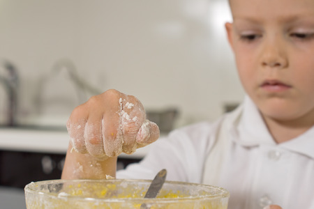Little boy busy baking a cake adding an ingredient into the eggs in the bowl with floury hands, close up of the handの写真素材