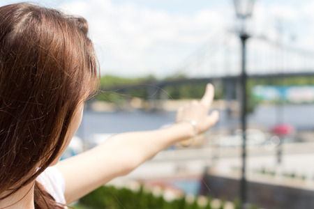 Side rear view of a brown haired female tourist pointing towards a remote bridge, during an interesting city-breakの写真素材