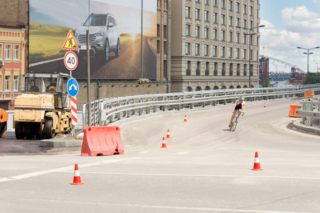 Cyclist corning off an urban overpass at speed riding past traffic warning cones and a barricade blocking a tarring machine and roadworksの写真素材