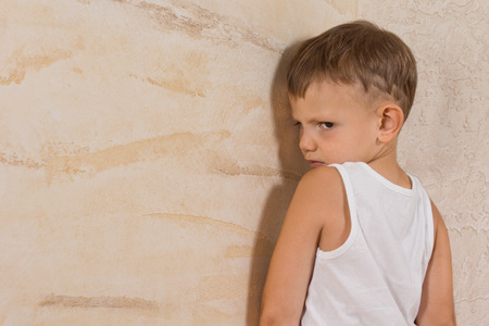 Cute Little Mad Boy Wearing White Undershirt Isolated on Light Brown Wallsの写真素材