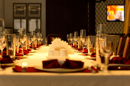 Dining table set with elegant place settings with red linen accents for a formal party or celebration in a restaurant or club, low angle view down the length of the tableの写真素材