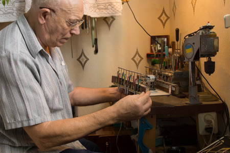 Old Man in Gray Polo Innovating Electronic Device on Small Brown Platform.