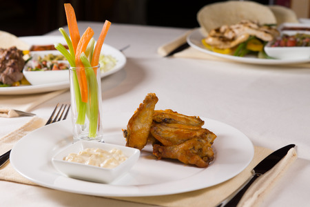 Chicken Wings with Vegetables and Dip at Place Setting on Restaurant Tableの写真素材