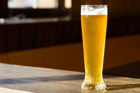 Tall Glass of Beer in Sunray on Tableの写真素材