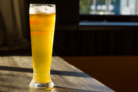 Tall Glass of Beer on Table with Sun Streaming Through Windowの写真素材