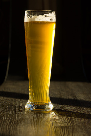Tall Glass of Beer on Table in Streaming Sunlightの写真素材