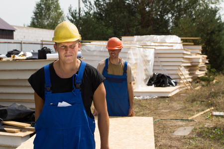 Construction workers carrying insulated wooden wall panels on a building site approaching the cameraの写真素材