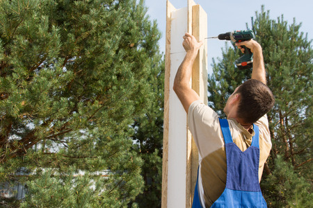 Young Male Manual Worker Drilling a Wooden Post at the Construction Site.の写真素材