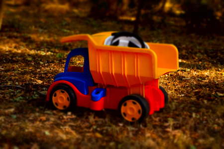 Colorful plastic toy dumpster truck with a hardhat in the back standing on the ground outdoors in the garden in the shade of a tree, side viewの写真素材