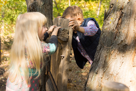 Laughing little boy and girl playing with an old rustic wooden gate attached to a tree trunk pushing against each other from opposite sidesの写真素材