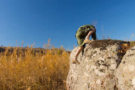 Boys Scout Climbing on Big Old Rock at the Brown Field Under a Blue Sky During Autumn Season.の写真素材