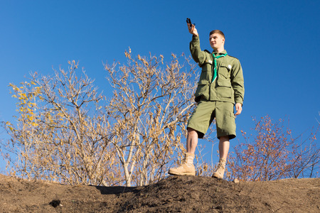 Scout standing on a rock taking a compass reading to get his bearing and location, low angle skyline...