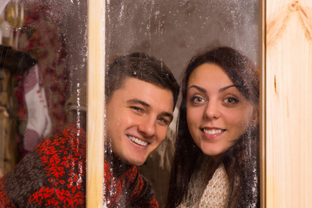 Close up Happy Young Couple in Winter T-Shirts Smiling Behind Glass Windows While Looking at the Camera.の写真素材