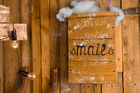 Old wooden handmade mailbox mounted on the exterior wall of a rustic timber house, decorated with Christmas lights, in a snowy day of winterの写真素材