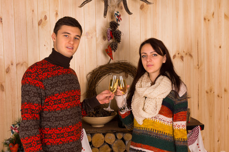 Young Partners in Casual winter Outfits Tossing Flute Glasses of Champagne Inside the House While Looking at the Camera.の写真素材