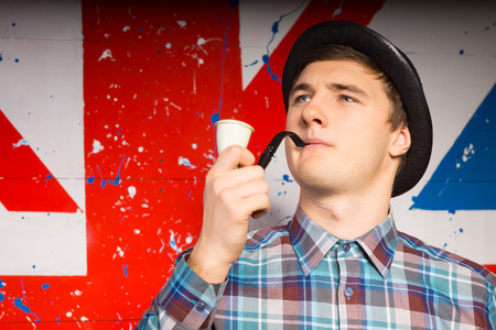 Low angle view of the stereotypical English gentleman wearing a bowler at and smoking a pipe against a backdrop of the union flagの写真素材