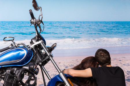 Loving couple enjoying a quiet day at the seaside sitting alongside their motorbike facing out over the ocean and waves on the golden sandの写真素材