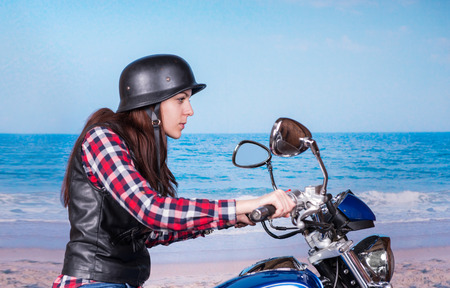 Profile View of Tough Young Woman Wearing Helmet Riding Past Beach on Motorcycleの写真素材