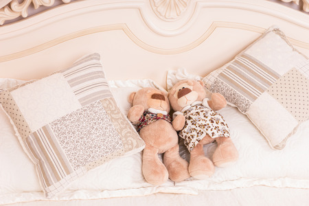 Male and Female Teddy Bear Couple Snuggling Amongst Cushions on Bedの写真素材
