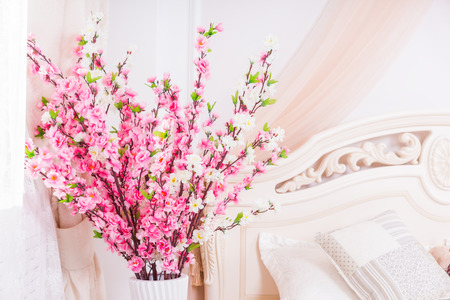 Pretty decoration of fresh pink spring blossom in a tall vase alongside a bedの写真素材