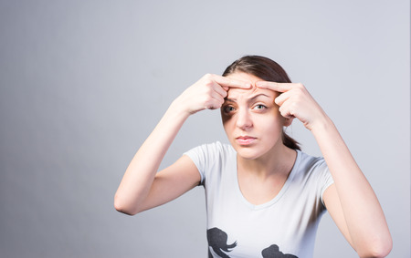 Close up Young Woman Pricking Pimple on her Forehead While Looking at the Camera Seriously. Captured...