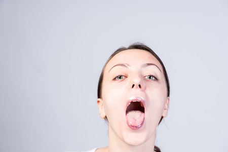 Close up Face of a Young Woman with Wide Open Mouth Looking at Camera on a Light Gray Background.の写真素材