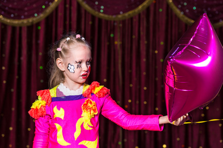 Talented blond girl performing with colorful diadem and flowers painted on face and sewed on vivid pink theatrical costumeの写真素材
