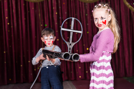 Boy and Girl Dressed as Clowns Standing on Stage with Red Curtain Holding Large Double Barrel Gun with Iron Sightの写真素材