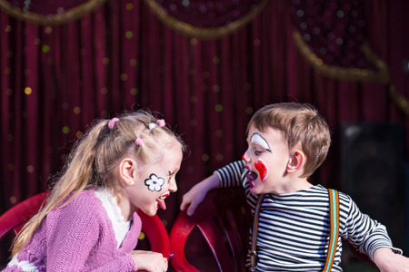 Cute funny boy and girl with painted faces acting as a couple with communication problems, during a theatrical performanceの写真素材