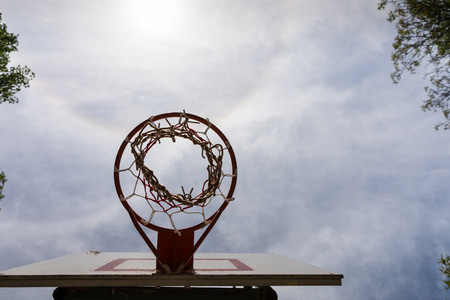 Low Angle View of Basketball Backboard, Basket, and Net Against Sunny Blue Sky with Clouds, Directly Underneath Basketball Hoop with Copy Spaceの写真素材
