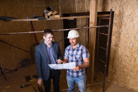 High Angle View of Young Male Architect and Construction Worker Foreman Inspecting Building Plans...