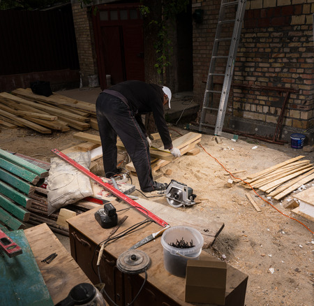 High Angle View of Man Using Hand Held Power Saw to Cut Planks of Wood for Home Construction Leaving Piles of Saw Dust on Floor of Outdoor Job Siteの写真素材