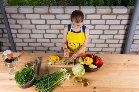 Young girl chopping and dicing fresh farm vegetables at a large outdoor table in front of a brick wallの写真素材